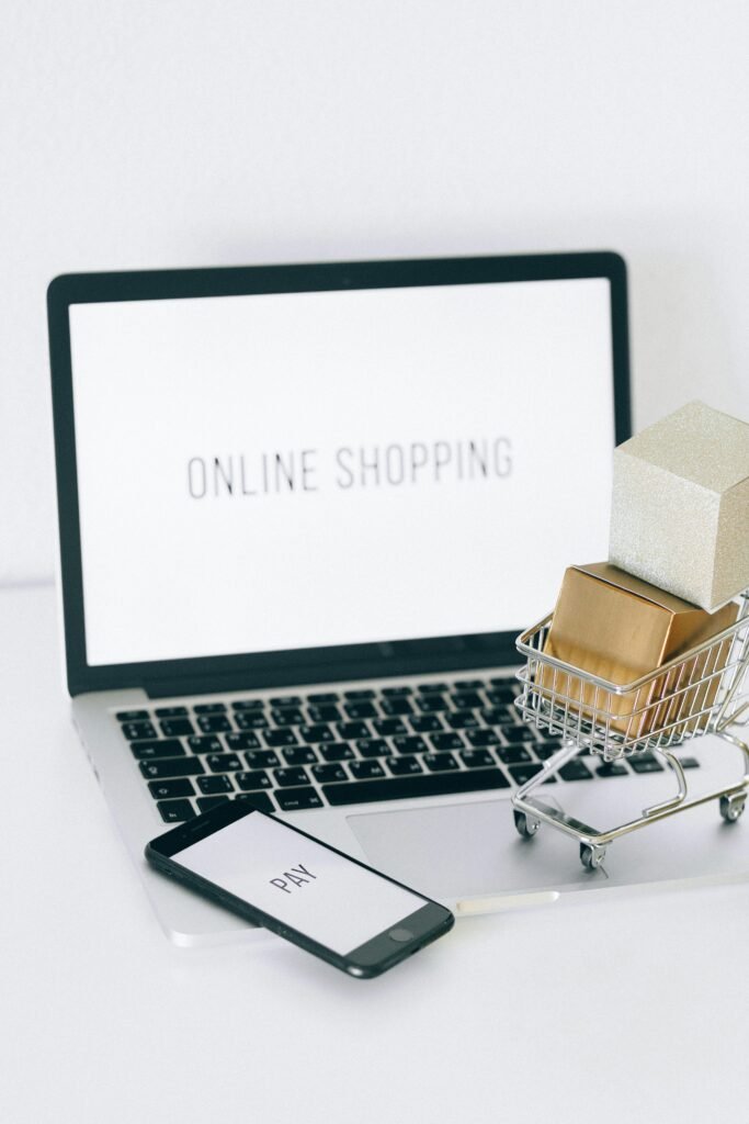 pexels-photo-6214479-6214479 Minimalist setup showcasing online shopping with a laptop and miniature cart.
